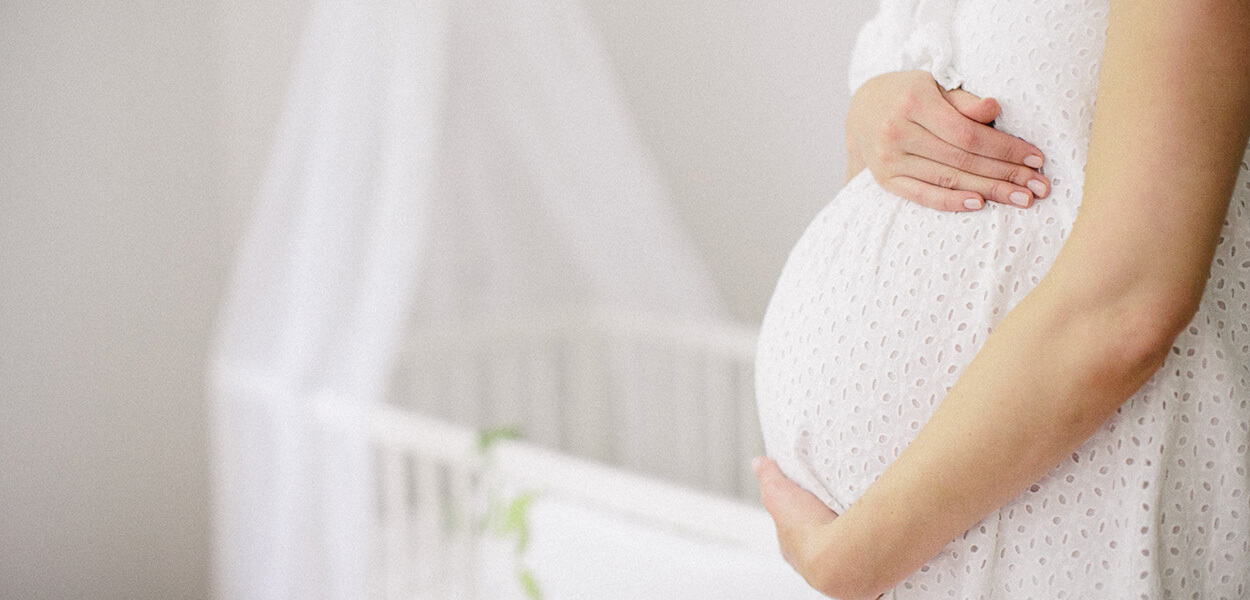 vimum_vorfreude-aufs-baby Werdende Mama umarmt liebevoll ihren schwangeren Bauch vor einer Wiege